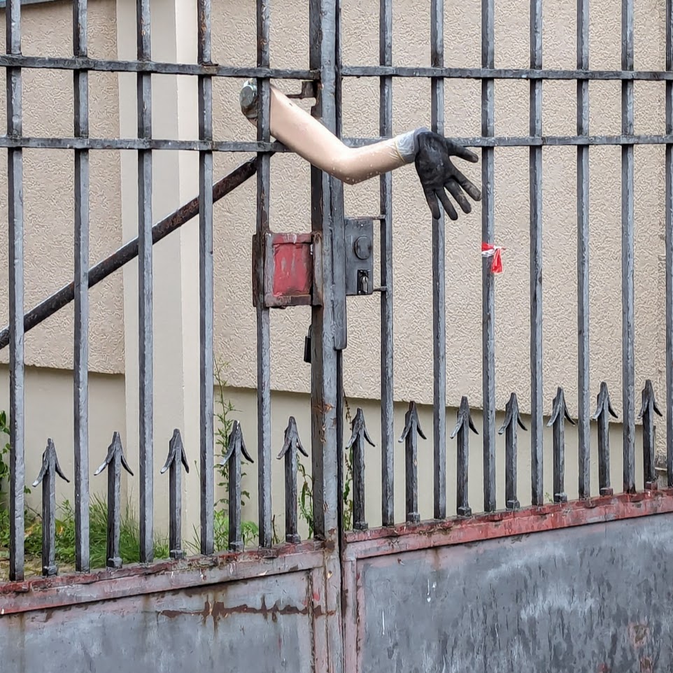 a mannequin arm with black paint on its palms and it's sticking in a metal fence. it's looks a bit surreal.